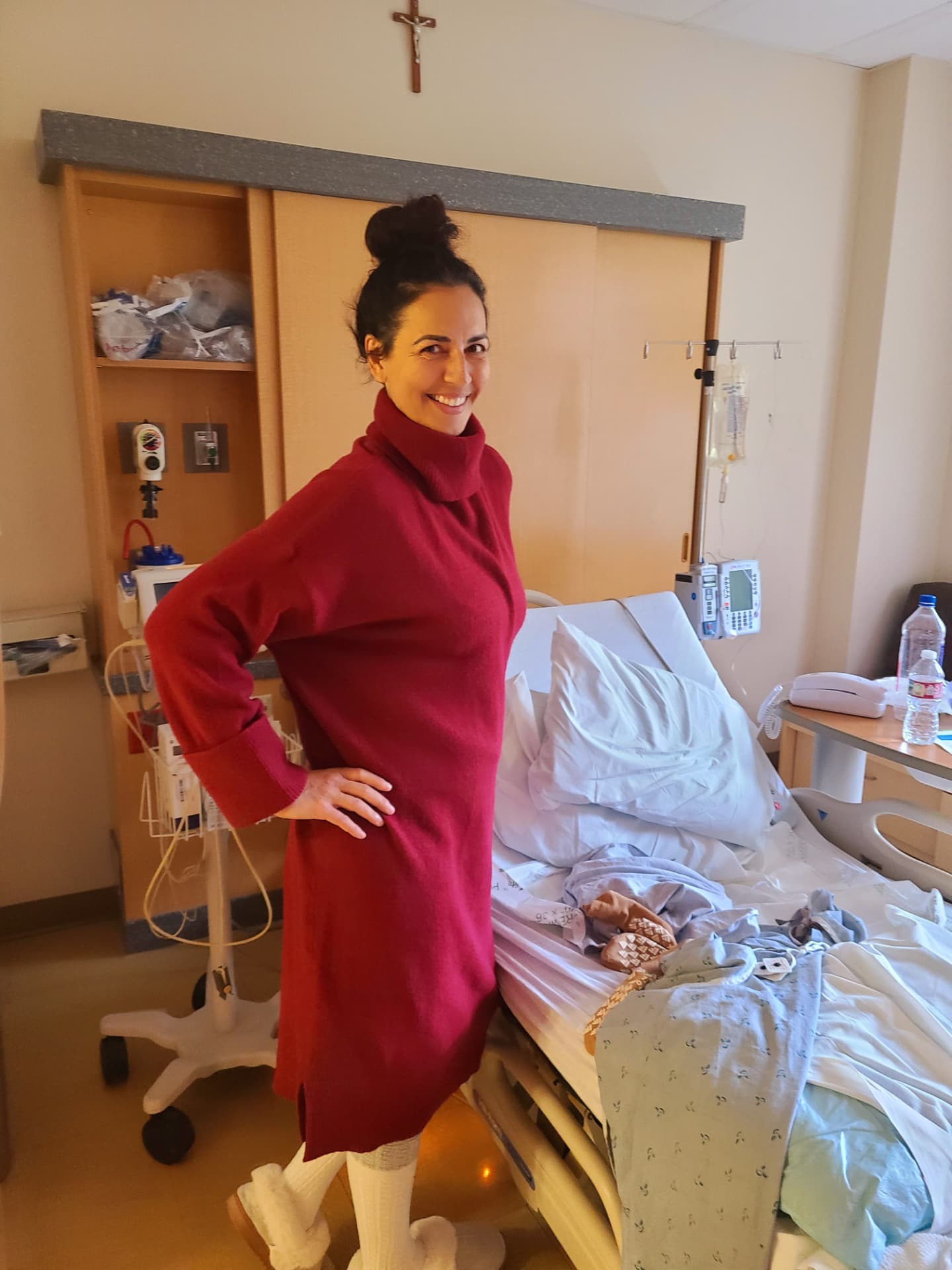Toni standing beside her hospital bed in a red sweater